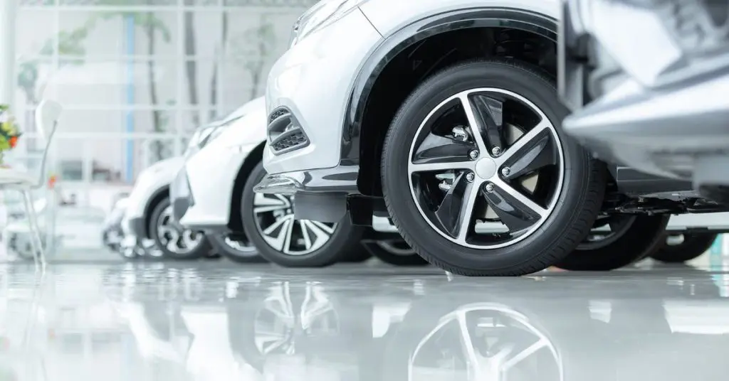 Payment assist supporting garages: A low-angle close-up of a row of silver cars with alloy wheels lined up on a polished showroom floor, with their reflections visible beneath them.