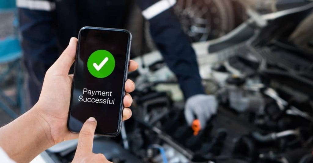 and holding a smartphone showing a successful payment screen, illustrating interest-free car repair finance through BNPL services.