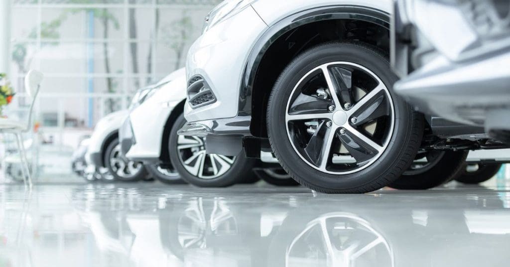 Payment assist supporting garages: A low-angle close-up of a row of silver cars with alloy wheels lined up on a polished showroom floor, with their reflections visible beneath them.