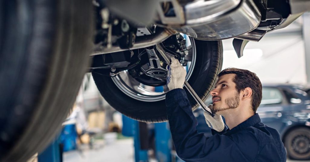 What makes car repair finance easy to use A mechanic in a garage using a wrench to work on the underside of a car raised on a lift.