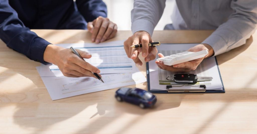 Why simple car repair finance leads to faster approvals Close-up of two people at a desk reviewing financial documents with a calculator, pen and toy car, alongside a set of car keys on a clipboard.