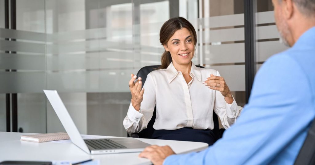 is a soft credit check bad for my score: Smiling businesswoman in a white blouse talking with a client across a desk in a glass-walled office.